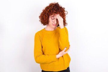 Fototapeta na wymiar young redhead girl wearing yellow sweater over white background making facepalm gesture while smiling amazed with stupid situation.