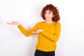 young redhead girl wearing yellow sweater over white background Inviting to enter smiling natural with open hands. Welcome sign.