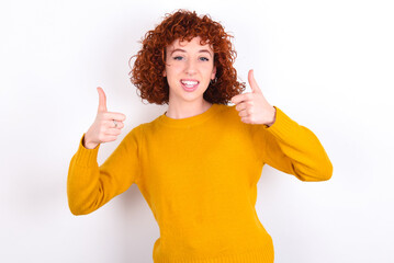 Optimistic young redhead girl wearing yellow sweater over white background showing thumbs up with positive emotions. Quality and recommendation concept.
