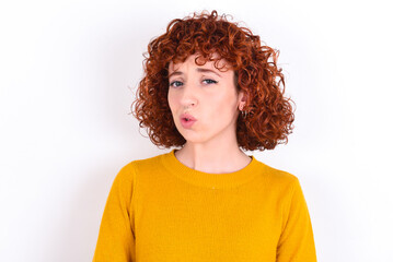 young redhead girl wearing yellow sweater over white background expressing disgust, unwillingness, disregard having tensive look frowning face, looking indignant with something.