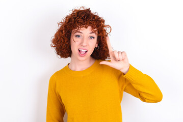 Pleasant looking young redhead girl wearing yellow sweater over white background has clever...