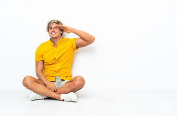 Fototapeta premium Young English man sitting on the floor saluting with hand with happy expression