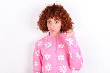 young redhead girl wearing pink floral t-shirt over white background shows fist has annoyed face...
