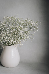 White flowers in white vase on white and grey background 