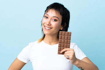 Young Uruguayan woman over isolated blue background taking a chocolate tablet and happy