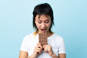 Young Uruguayan woman over isolated blue background eating a chocolate tablet