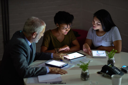 Combining their technical knowhow. Shot of a group colleagues using digital tablets while working late in an office. - Powered by Adobe