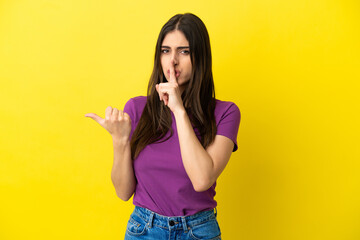 Young caucasian woman isolated on yellow background pointing to the side and doing silence gesture