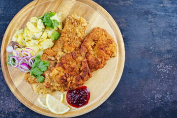 Traditionelles frittiertes Schnitzel mit Zitronenscheiben und Zwiebelringen serviert als close-up auf einem Holzbrett mit Textfreiraum rechts