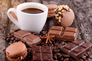 cup of coffee with chocolate, macaroons  and coffee beans on wooden background