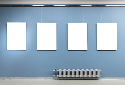 Four blank white vertical posters hang on blue wall