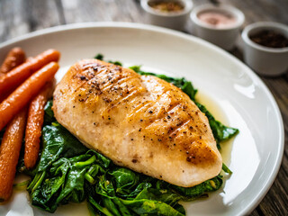 Fried chicken breast with spinach and carrots on wooden table