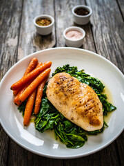 Fried chicken breast with spinach and carrots on wooden table