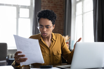 Worried frustrated Black professional woman reading paper notification with bad news, getting...