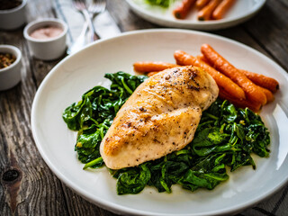 Fried chicken breast with spinach and carrots on wooden table
