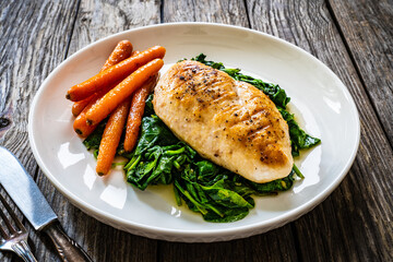 Fried chicken breast with spinach and carrots on wooden table