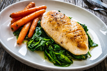 Fried chicken breast with spinach and carrots on wooden table
