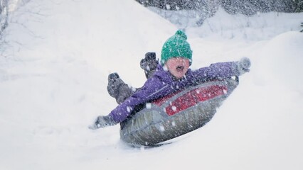 Cute child boy riding on snow tubing rising hands up. Kid sledding slide down hill. Winter fun activity outdoor.