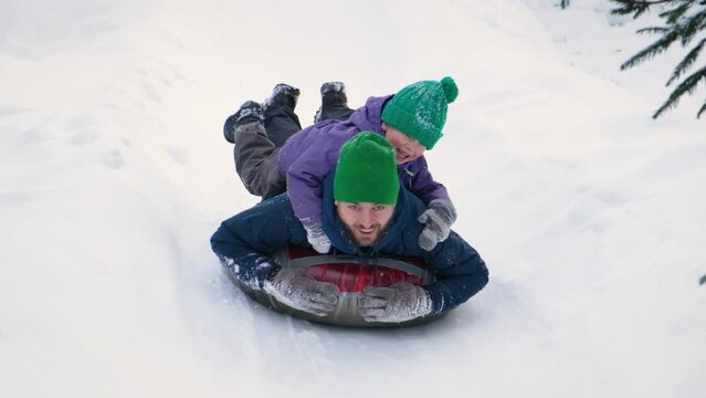 Snow tubing, winter family activity. Happy exited father and son riding on inflatable tube together. Parent and kid sledding slide down hill.