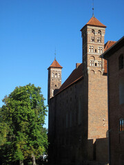 Fototapeta na wymiar Beautiful view of a medieval castle with brick walls, towers, tiled roof in architectural Gothic style in an old town in Poland. A quiet, calm, sunny summer day. 