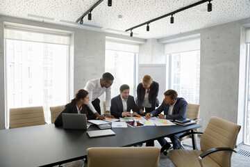 Concentrated successful happy diverse colleagues analyzing financial paper documents at briefing meeting, developing corporate growth strategy or discussing marketing research results in modern office