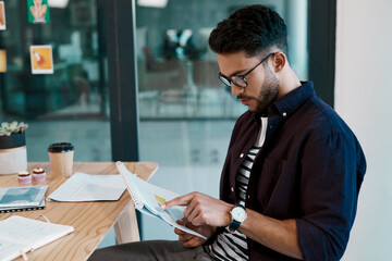 Always going through paperwork. Cropped shot of a handsome young businessman wearing spectacles and sitting alone in his office while reading paperwork.