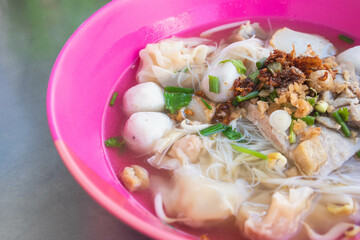 Noodles and clear soup with pork dumplings, meatballs, and pork in a pink bowl