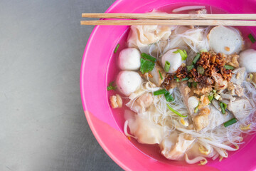 Noodles and clear soup with pork dumplings, meatballs, and pork in a pink bowl