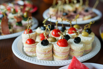 The buffet at the reception. Assortment of canapes on wooden board. Banquet service. Catering, snacks with different types of cheese and meat. Party Concept.