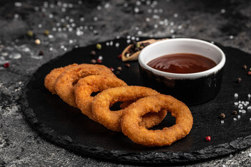 Homemade crunchy fried onion rings with tomato sauce on stone board, american unhealthy calories meal. Delicious pub style, appetizer, restaurant menu, top view