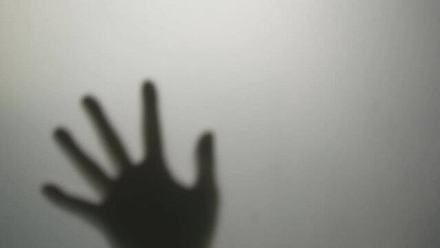 shadow people hand or human palm try to hits and breaks smashing on window frosted glass or wall door for need help to near death from murder assassin and dark ghost horror concept in restroom at home