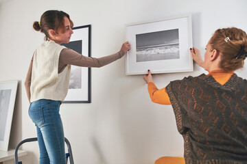 Mother and daughter hanging pictures and photos at home.