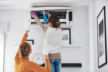Mother and daughter cleaning aircon filters indoor unit at home.