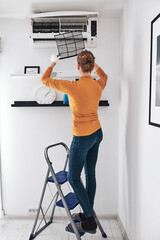 Woman cleaning aircon filters indoor unit at home.