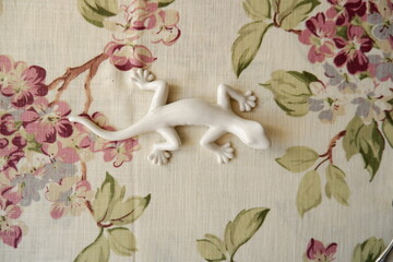 A white ceramic lizard on a vintage floral cloth.