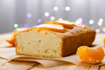Moist orange fruit pound cake on parchment with slices of orange and bokeh lights on background. Delicious breakfast, delights for tea time. Recipe of orange pie loaf.