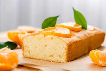 Moist mandarin pound cake on parchment with pieces of fresh tangerine on rustic wooden background....