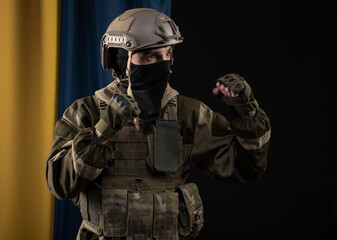 a male soldier in a military uniform and helmet on the background of the national flag of Ukraine