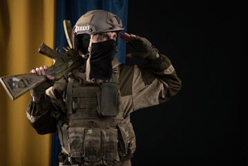 a male soldier in a military uniform and helmet with a weapon on the background of the national flag of Ukraine