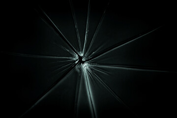 The hole in the broken and cracked glass on black background, closeup