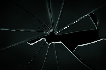 The hole in the broken and cracked glass on black background, closeup