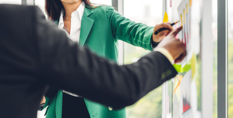 Fototapeta premium Casual creative happy two smile asian business people plan strategy analysis and brainstorm putting post it sticker note to share idea for startup project on glass board at modern office