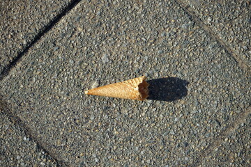 Reste der Waffel einer leeren angebissenen Eistüte auf grauem Straßenpflaster im Frühling bei...