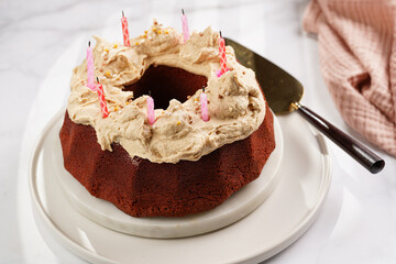 A red velvet bundt cake with liquor icing and birthday candles on white plate on marble surface