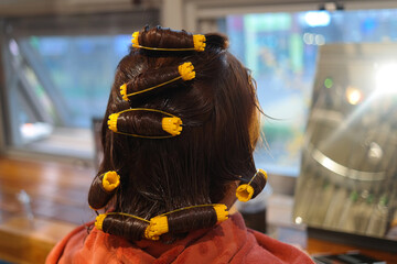 The back of a woman rolling her hair using beauty tools.