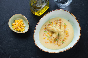 Cream-soup made of baby corn and served in a green bowl, high angle view on a black stone background