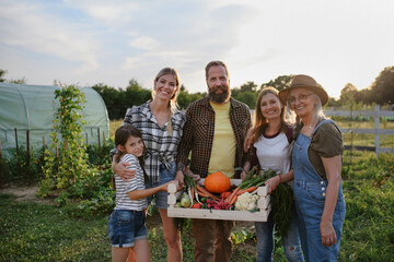 Happy farmer family looking at camera and holding their harvest outdoors in garden.