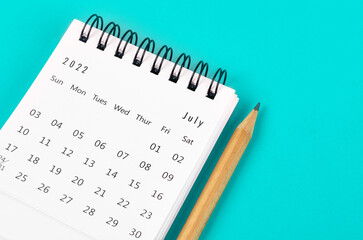 July 2022 desk calendar with wooden pencil on light blue background.