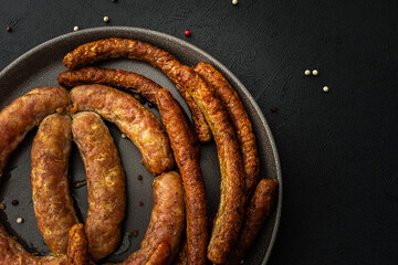 Baked pork sausages with spices in a plate close-up on a dark background