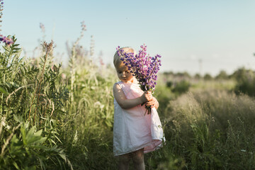 a child walks in a field with a bouquet of flowers - obrazy, fototapety, plakaty